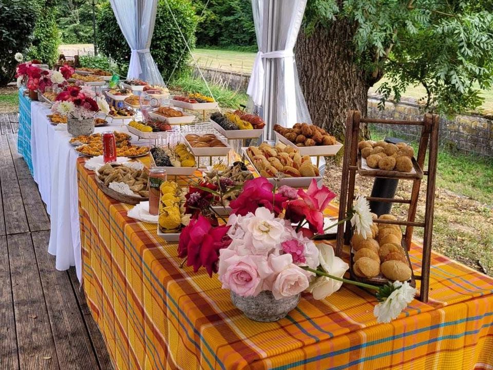 Une longue table de buffet couverte de plateaux, nappe madras orange et jaune.