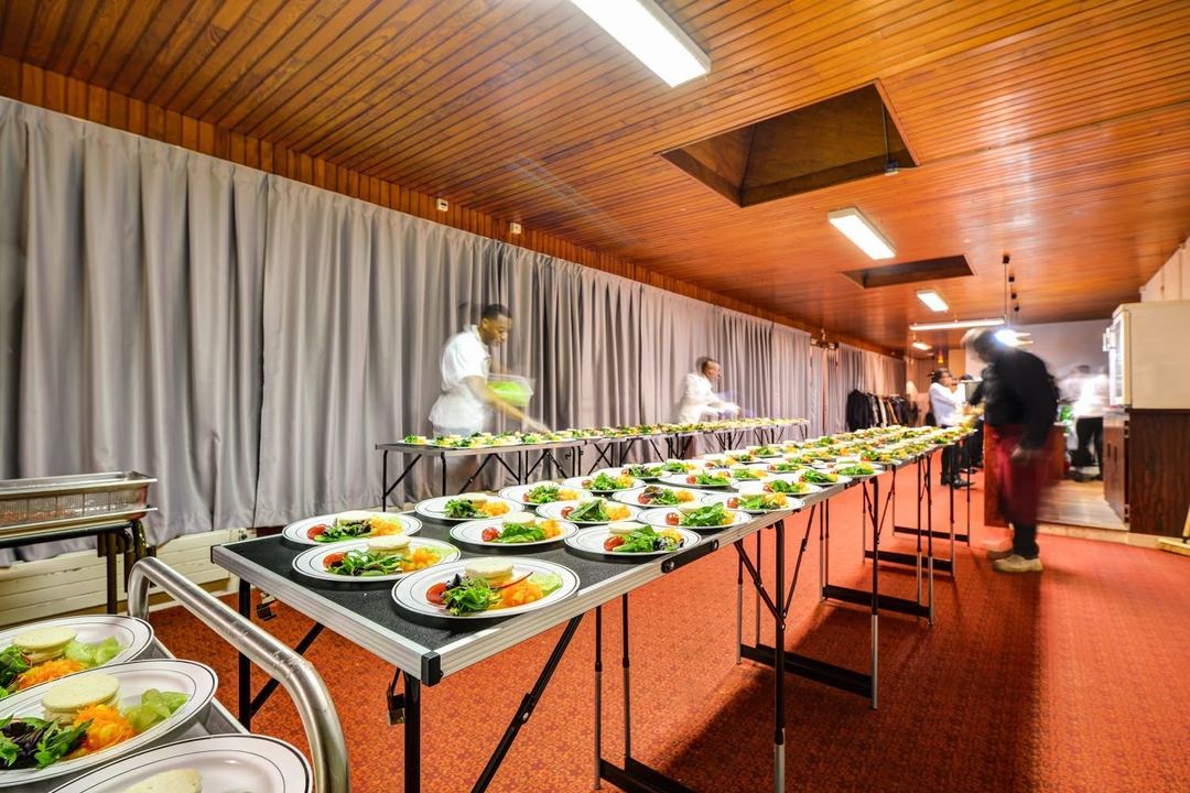 Dans une salle, de longues tables couvertes de dizaines d'assiettes d'entrées déjà dressées, que l'équipe finit de préparer.
